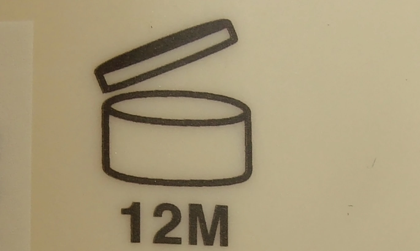 Close-up of a real cosmetic bottle showing an open-jar 12M period-after-opening symbol