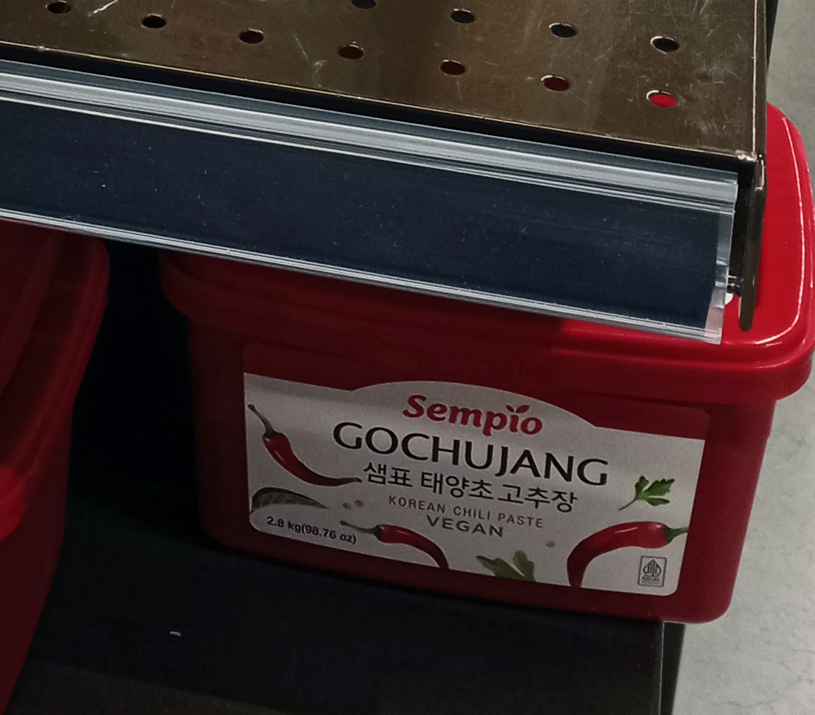 Rak toko dengan wadah gochujang merah yang menampilkan nama produk dan tulisan vegan; tidak ada status halal yang disimpulkan